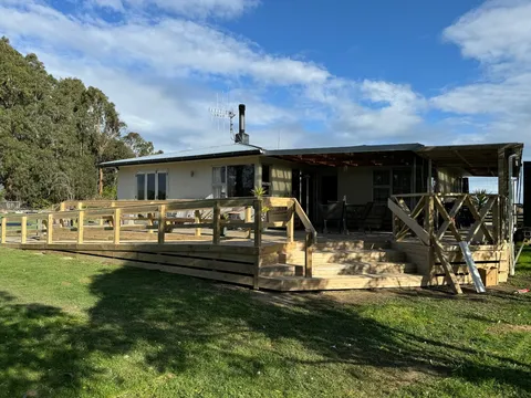 A wide timber deck with a balustrade and steps wrapped around the front of a single-storey house with a corrugated roof.