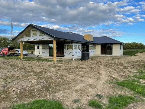 A house under construction with a dark roof, building wrap and cladding partly fitted, and timber posts supporting a front porch roof.