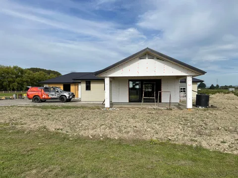 A house under construction with a covered entry, cladding partly fitted and a work ute parked on the gravel driveway.