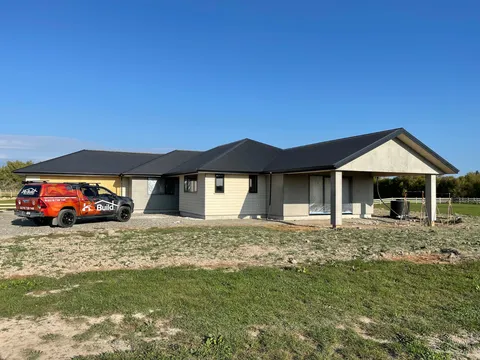 A single-storey house with a dark roof and cladding fitted, with a covered porch on the right and a work ute parked at the left.