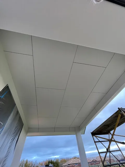 Looking up at the lined underside of a porch roof with white panels, with scaffolding and plastic sheeting at the edges.