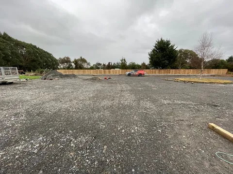 Cleared gravel area with piles of aggregate, a red ute and a tall timber fence along the back boundary.