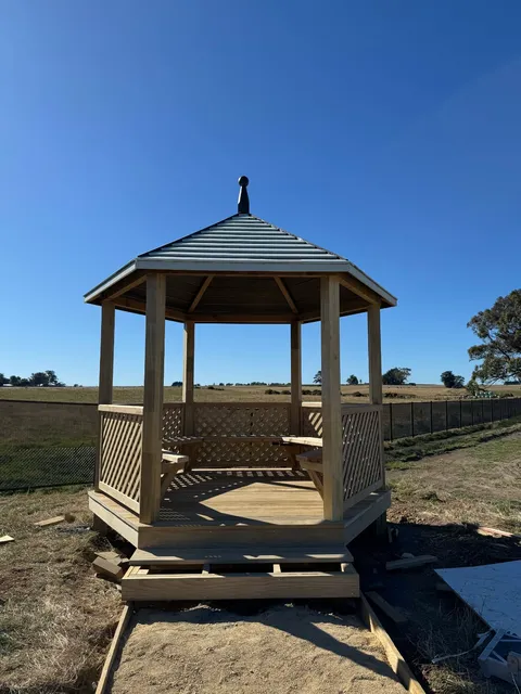 Six-sided timber gazebo with a metal roof, lattice side panels and a timber deck floor, seen from the front.