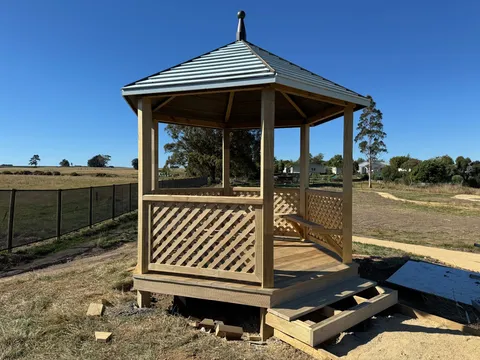 Timber gazebo with lattice panels, built-in bench seating, a metal roof and a stepped timber entry.