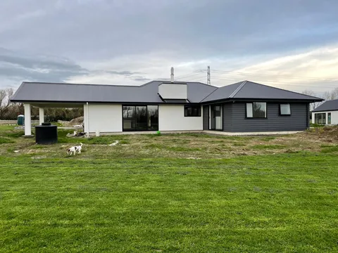 Single-storey house with dark grey cladding, white walls and a metal roof, with a lawn in the foreground.