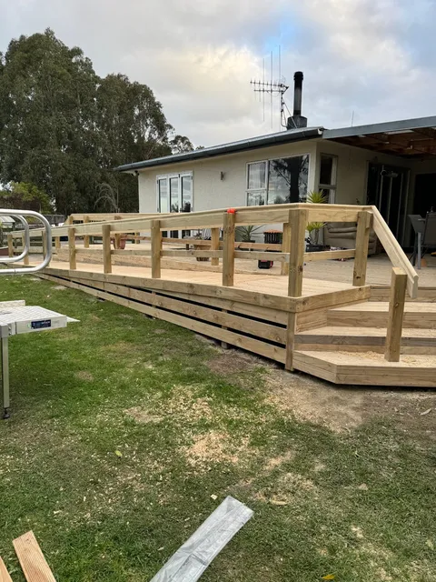 A long raised timber deck with a handrail and steps along the front of a house, still under construction.