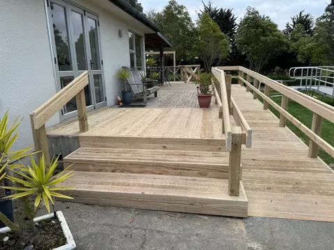A new timber deck with wide steps and a long ramp with handrails running beside it, leading to French doors.