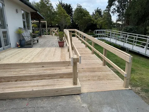A timber deck with steps and a handrailed timber ramp, with an aluminium ramp visible on the lawn in the background.